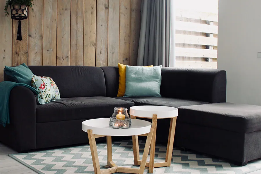 Wohnzimmer mit Holzwand, dunklem Sofa und runden Beistelltischen