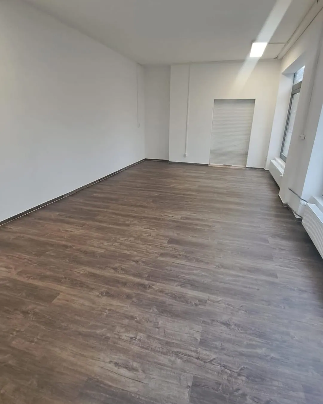 Nachher: Derselbe Raum fertig: weiße Wände, glatte Decke und neuer Vinylboden in Holzoptik
